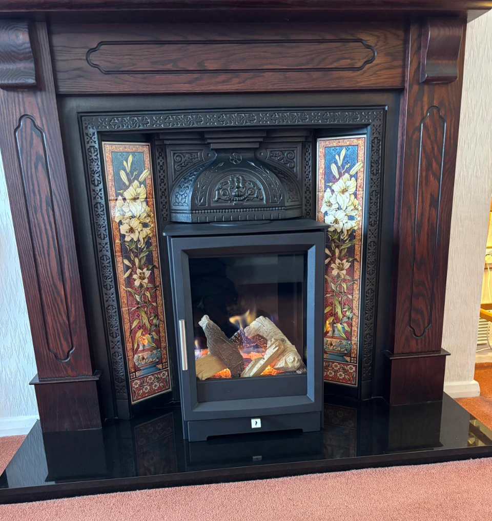 Dark wooden fireplace mantel with ornate tile surround and a black electric firebox on a glossy black hearth.