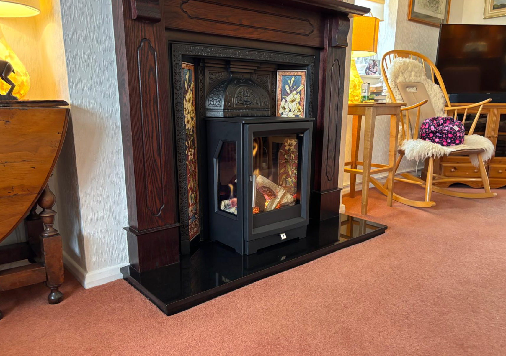 Fireplace with black stove insert and glowing flames in a cozy living room with carpet and wicker chairs