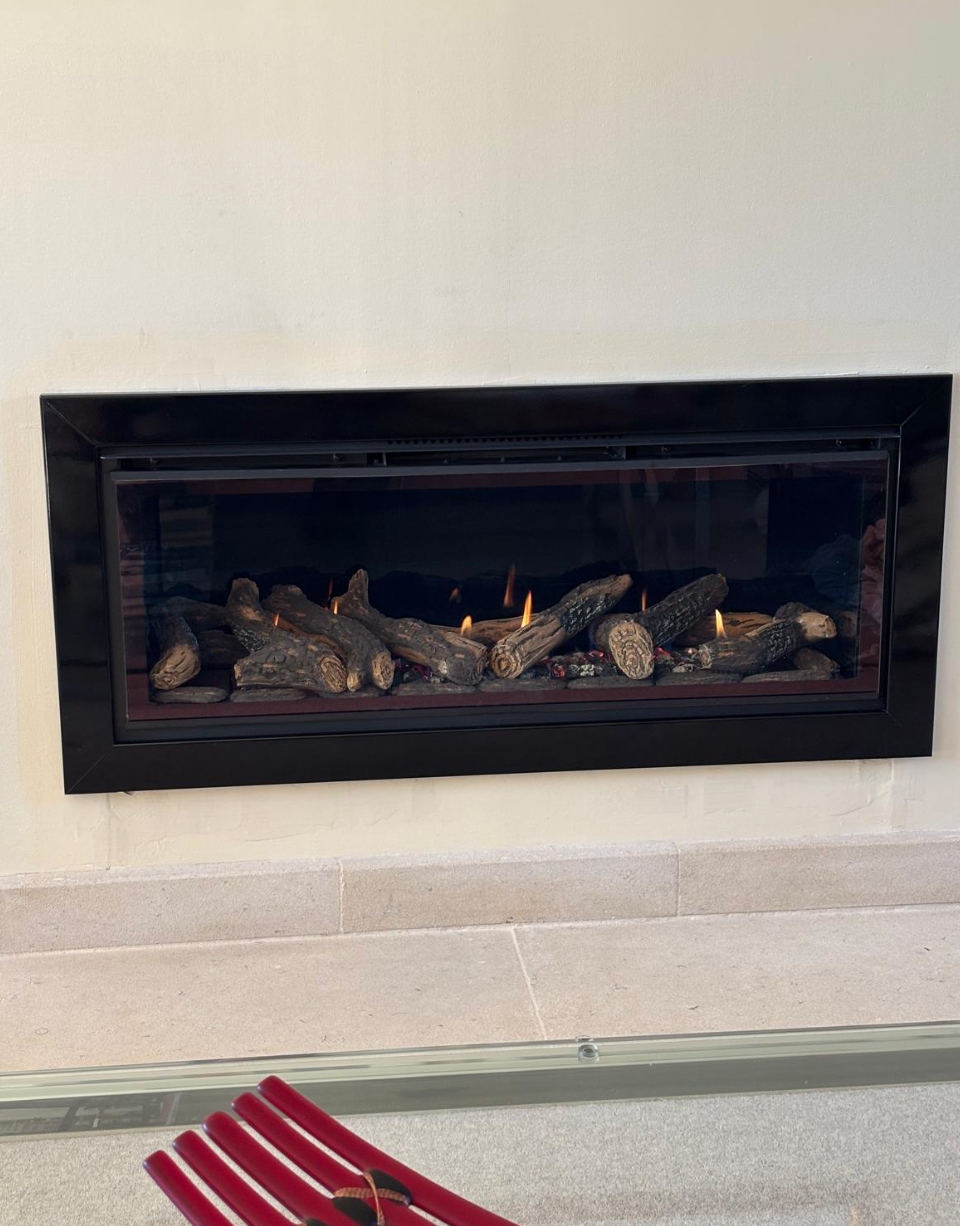 Wall-mounted black fireplace with decorative logs and a small flame above a beige hearth.