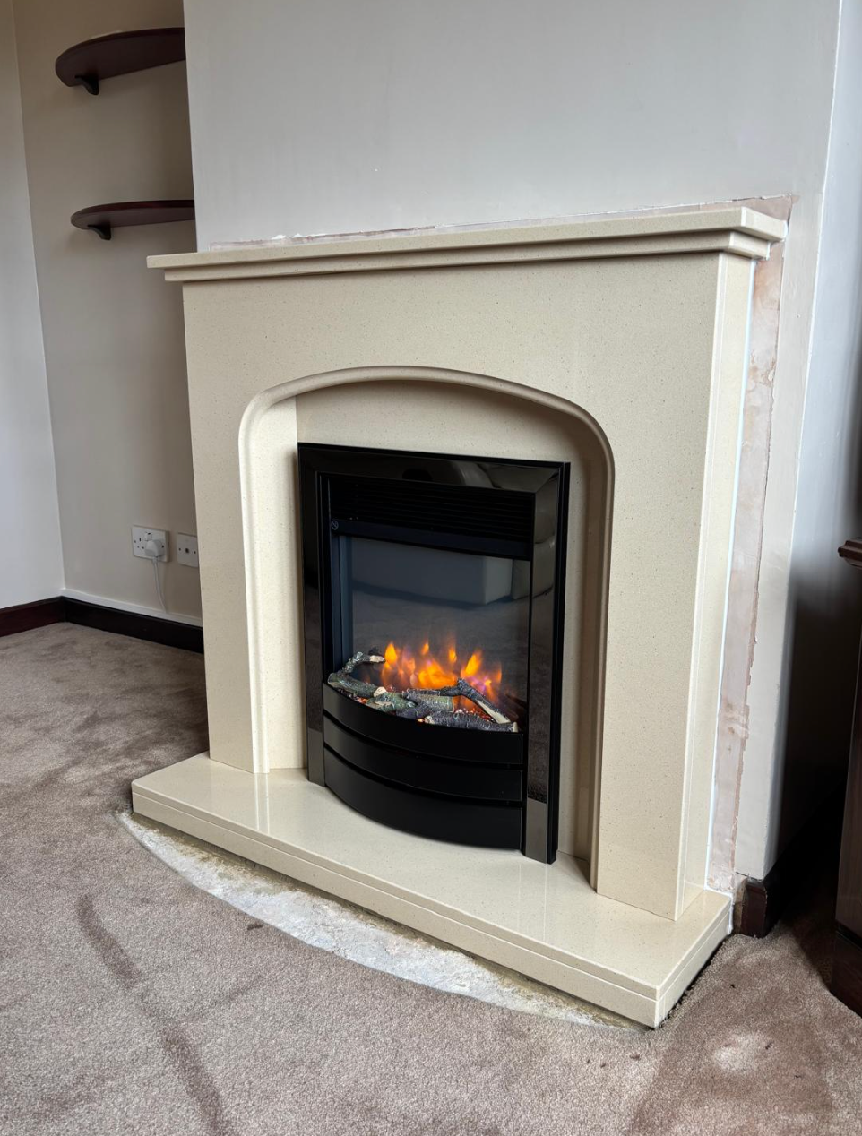Cream fireplace with a lit electric fire in a carpeted room.
