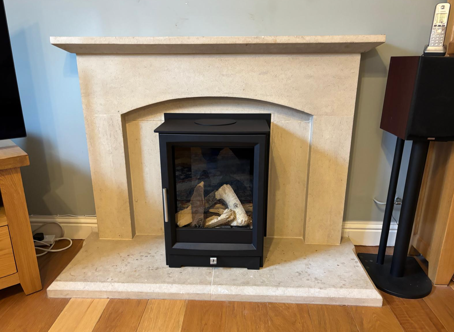 Beige stone fireplace surround with black electric stove centered on the hearth in a living room.