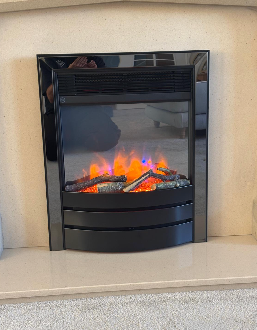 Black electric fireplace with orange flames built into a beige wall surround