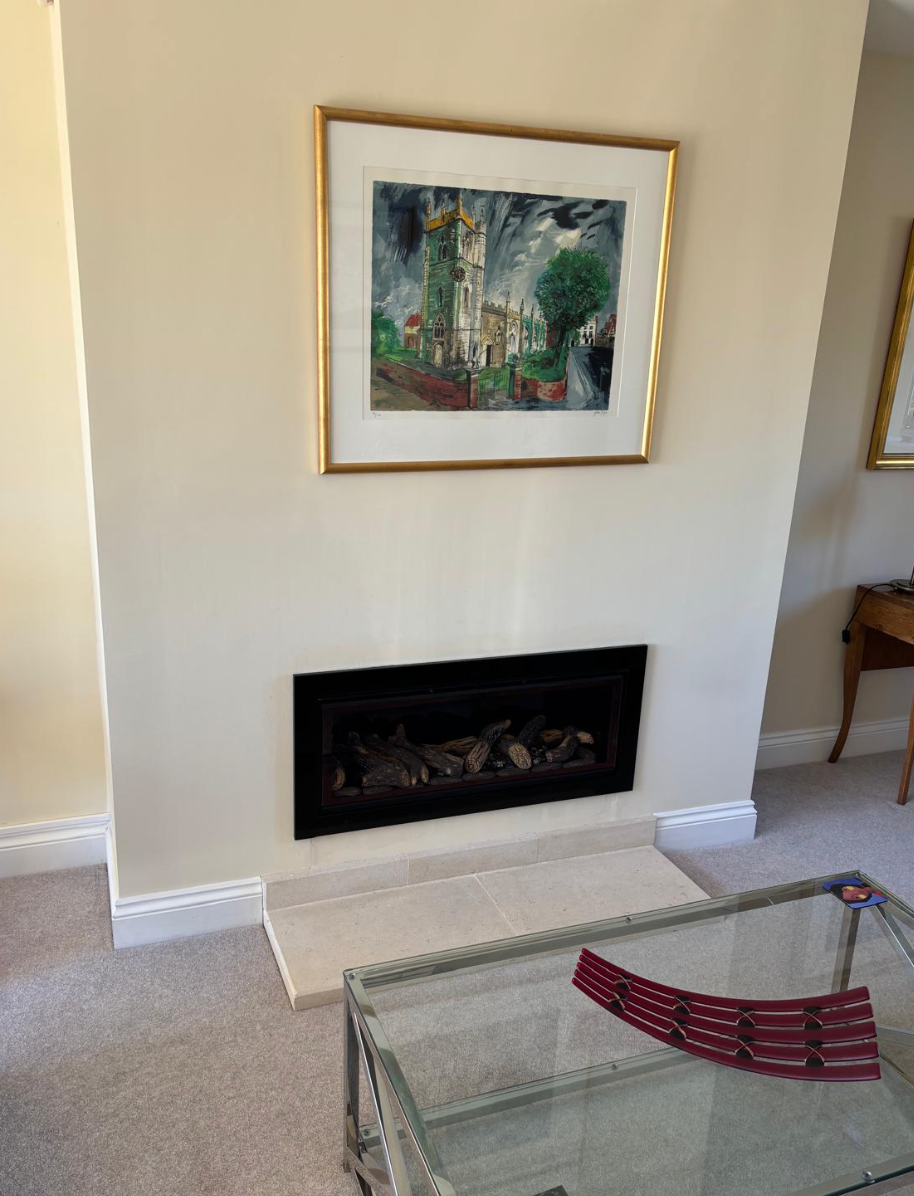 Living room wall with framed art above a black fireplace and a glass coffee table in front