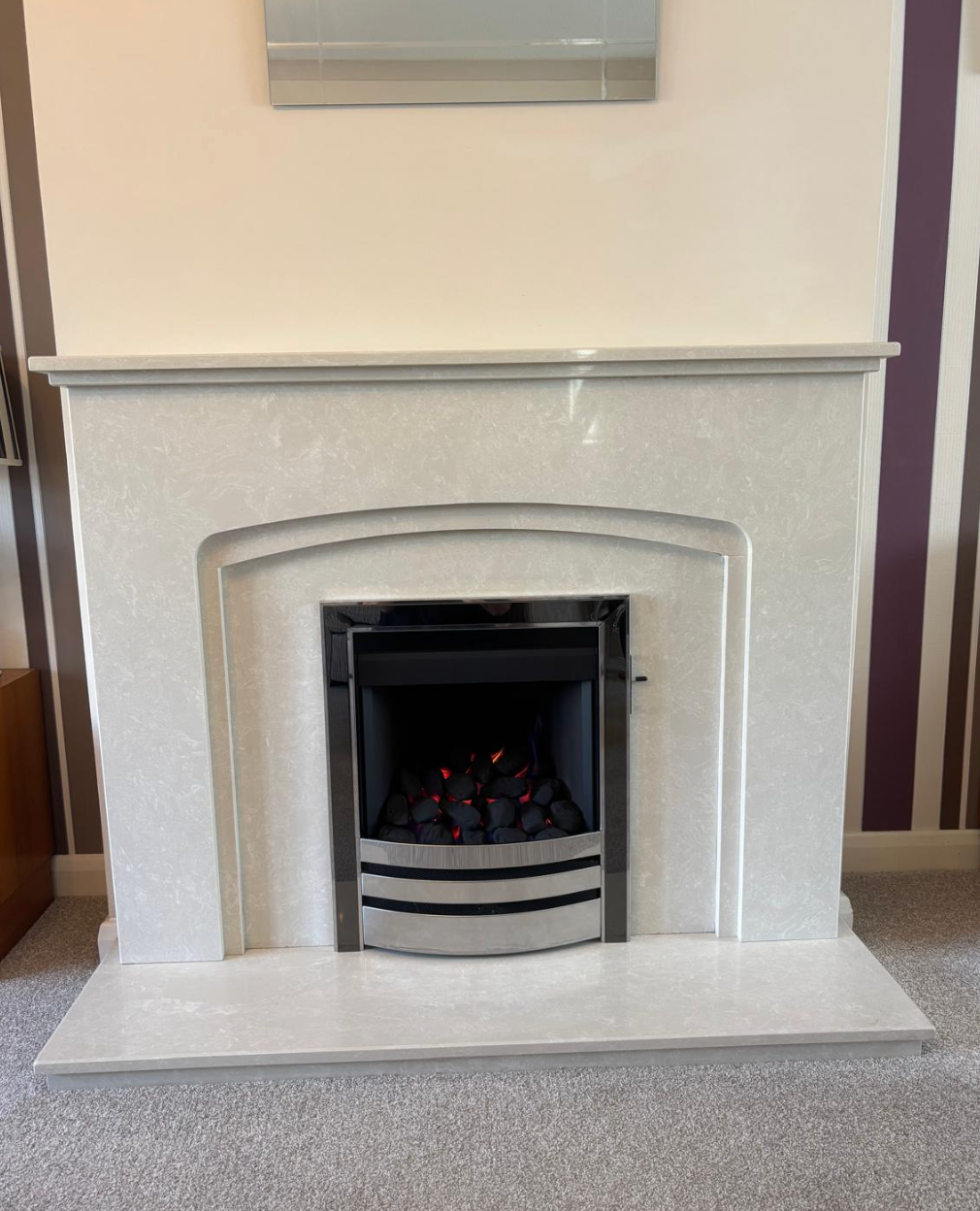 White decorative fireplace with a black electric fire insert in a beige room.