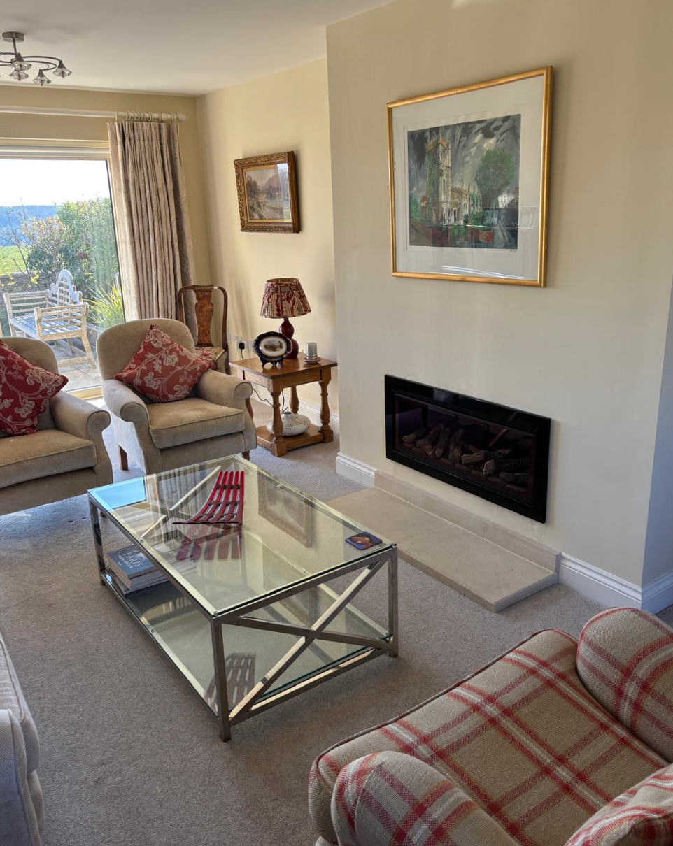 Living room with plaid sofas, glass coffee table, fireplace, and framed art by a sunny window
