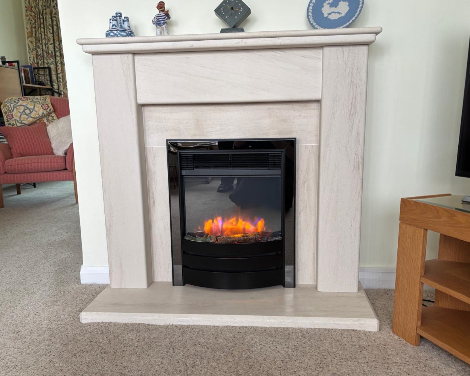 Cream fireplace with black electric fire and glowing flames in a carpeted living room