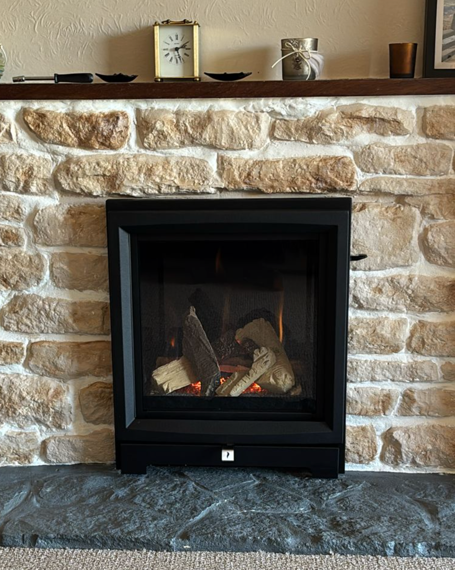 Stone fireplace with black insert and burning fire, topped by a wooden mantel with small decor items.