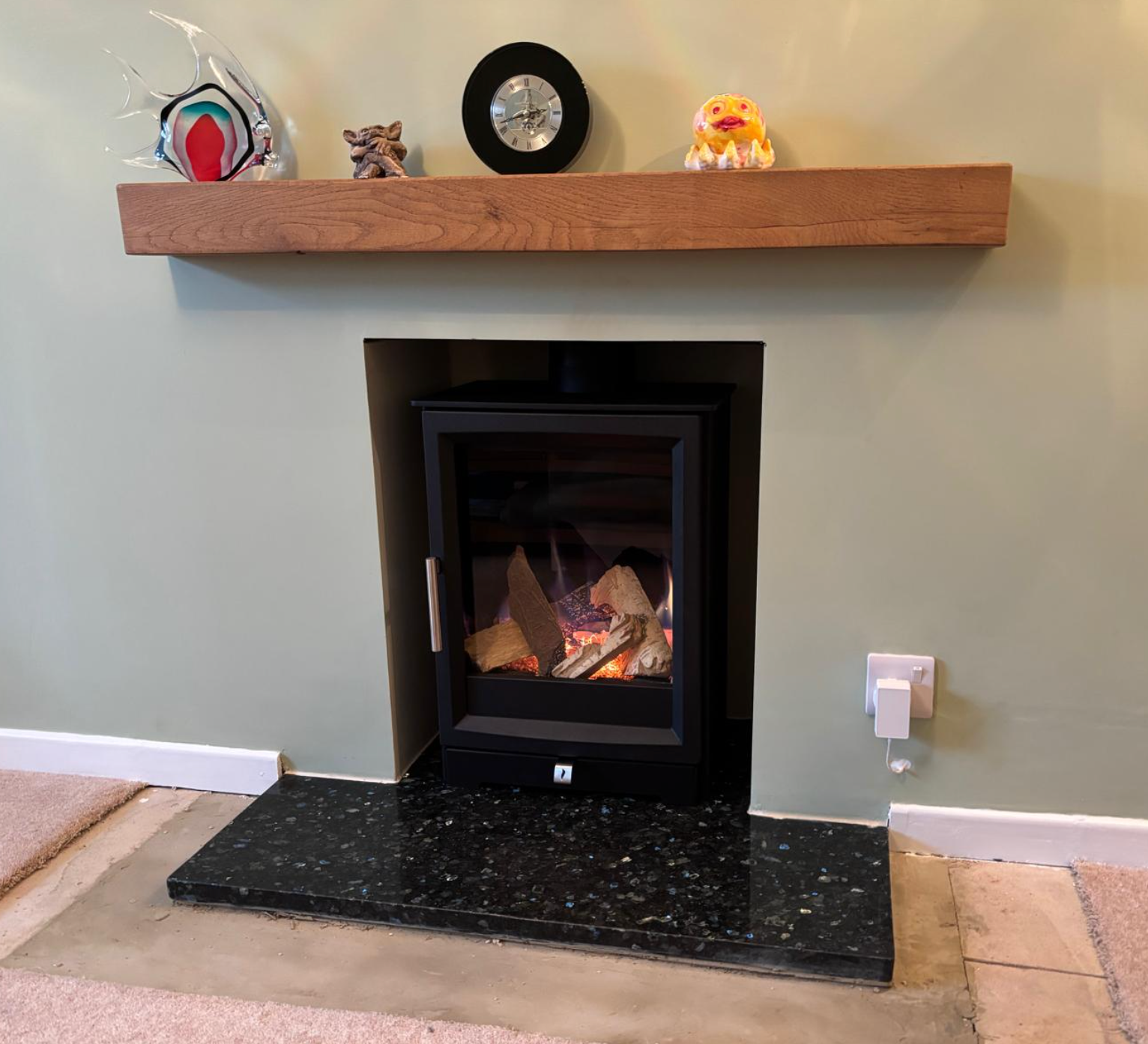 Modern fireplace with burning logs beneath a wooden mantel in a living room, framed by light walls and floor tiles