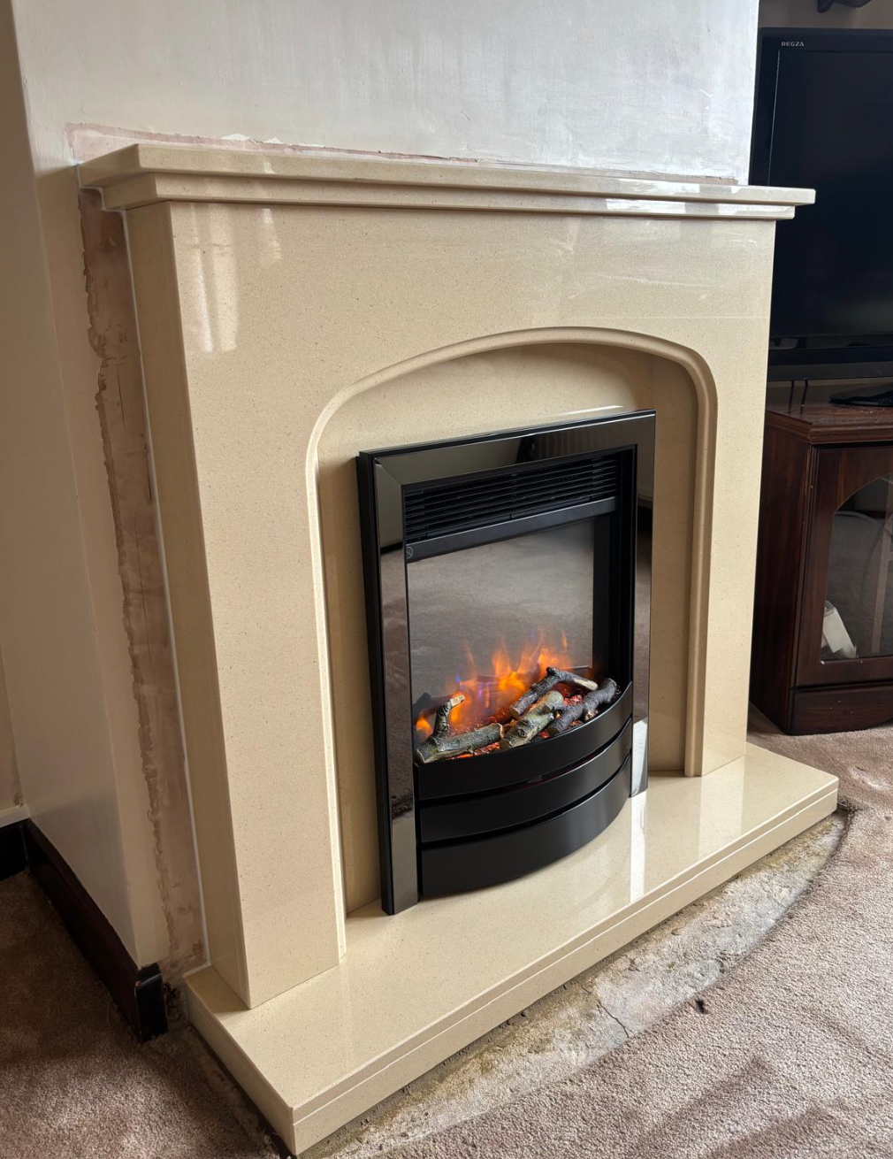 Beige electric fireplace with a glowing fire insert in a living room.