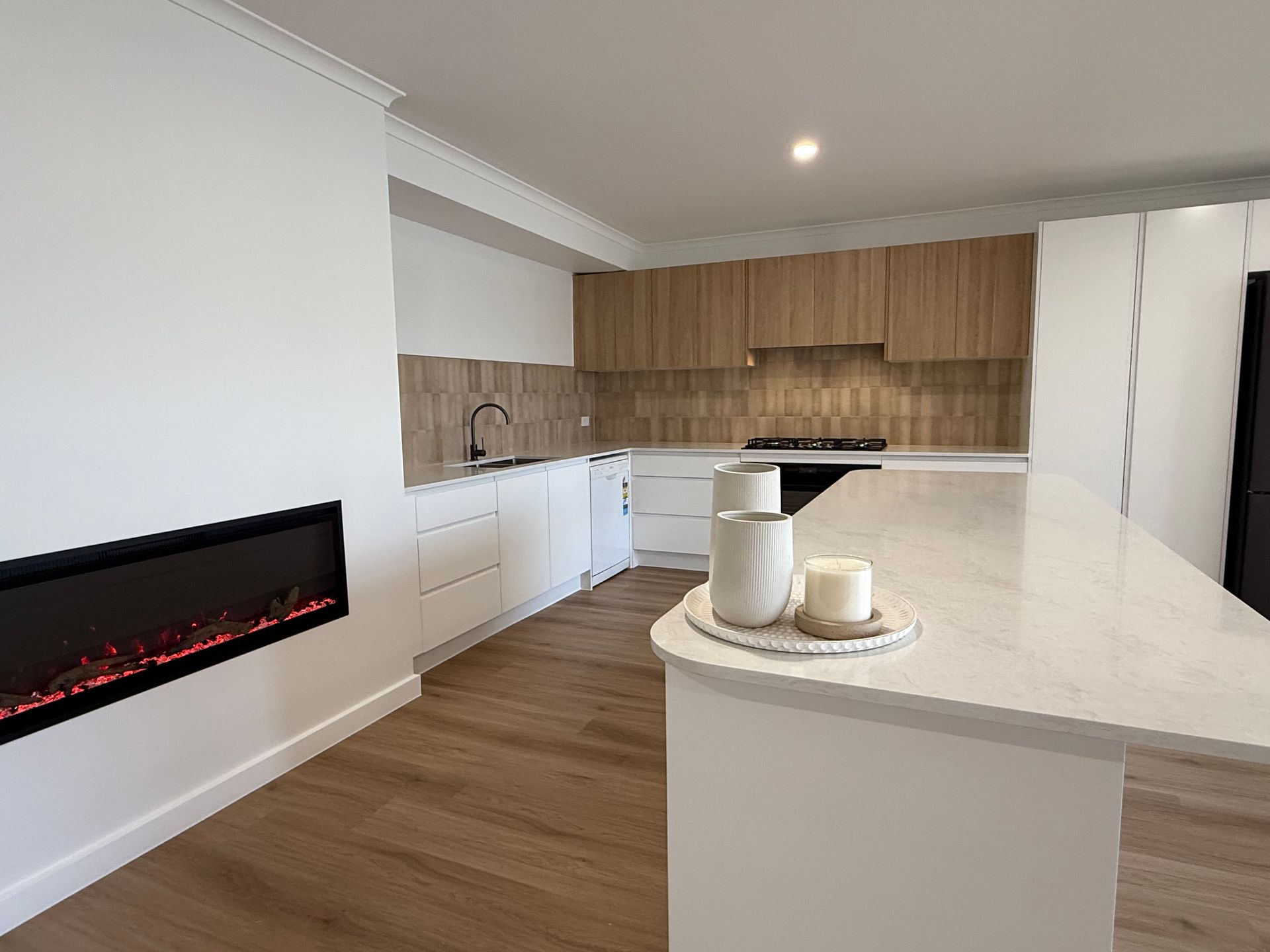 Modern kitchen with wood cabinetry, white island, and wall-mounted electric fireplace — LD Carpentry in Goulburn, NSW