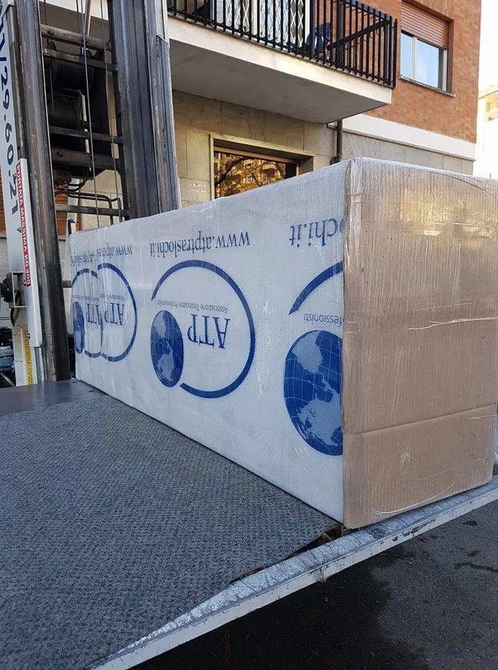 Pallet bianco avvolto in pellicola MLV su una rampa accanto all'ingresso di un condominio.
