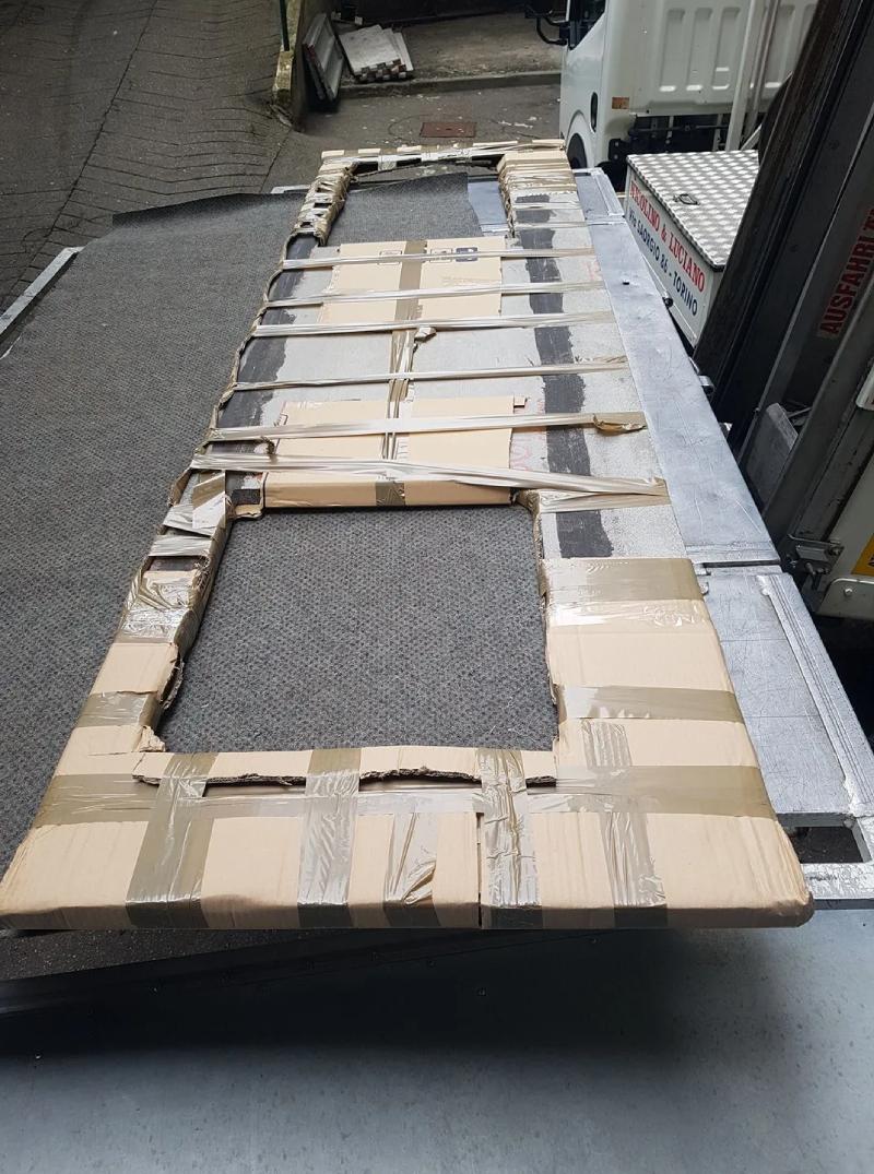 Pallet di scatole di cartone avvolte e nastro adesivo su un marciapiede accanto a un cordolo e a una ringhiera.