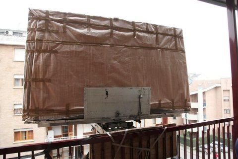 Un grande telone marrone copre una scatola su un balcone, con degli edifici sullo sfondo.