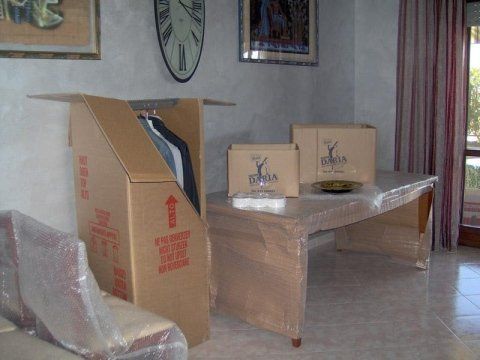 Scatole di cartone e mobili imballati in una stanza, a suggerire un trasloco o un deposito.