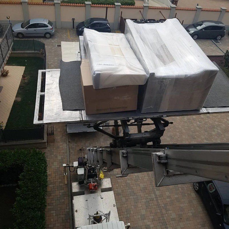 Un operaio su una piattaforma aerea solleva grandi scatole imballate da un cortile sottostante fino al tetto.