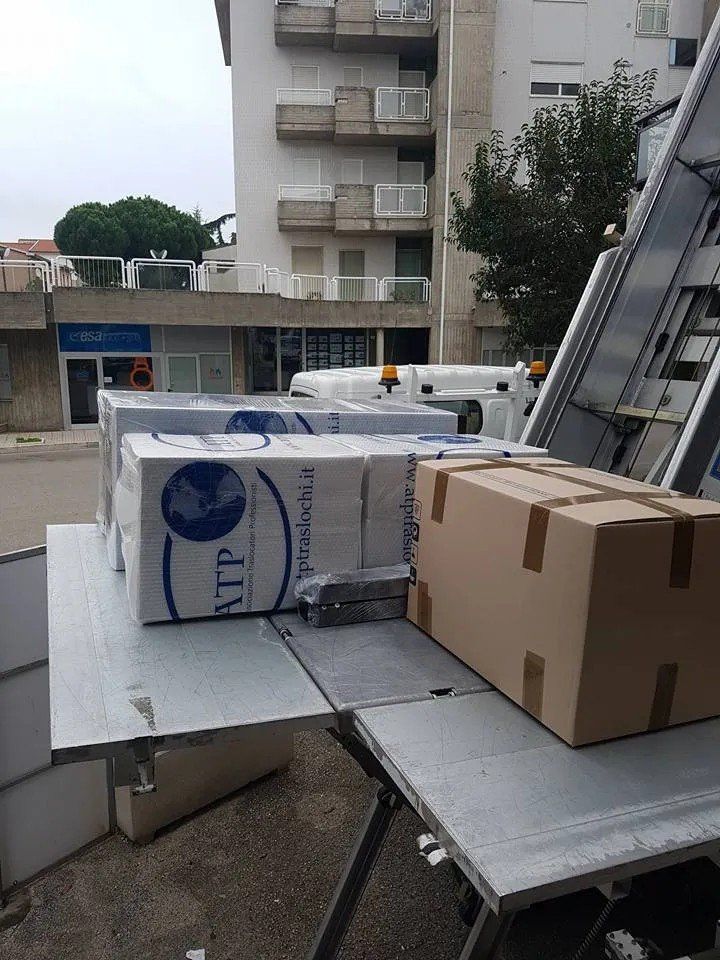 Scatole su una rampa di carico metallica accanto a un condominio, con un pallet avvolto nella plastica nelle vicinanze.