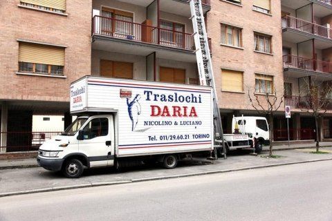 Un camion per le consegne è parcheggiato su una strada cittadina di fronte a dei palazzi residenziali.