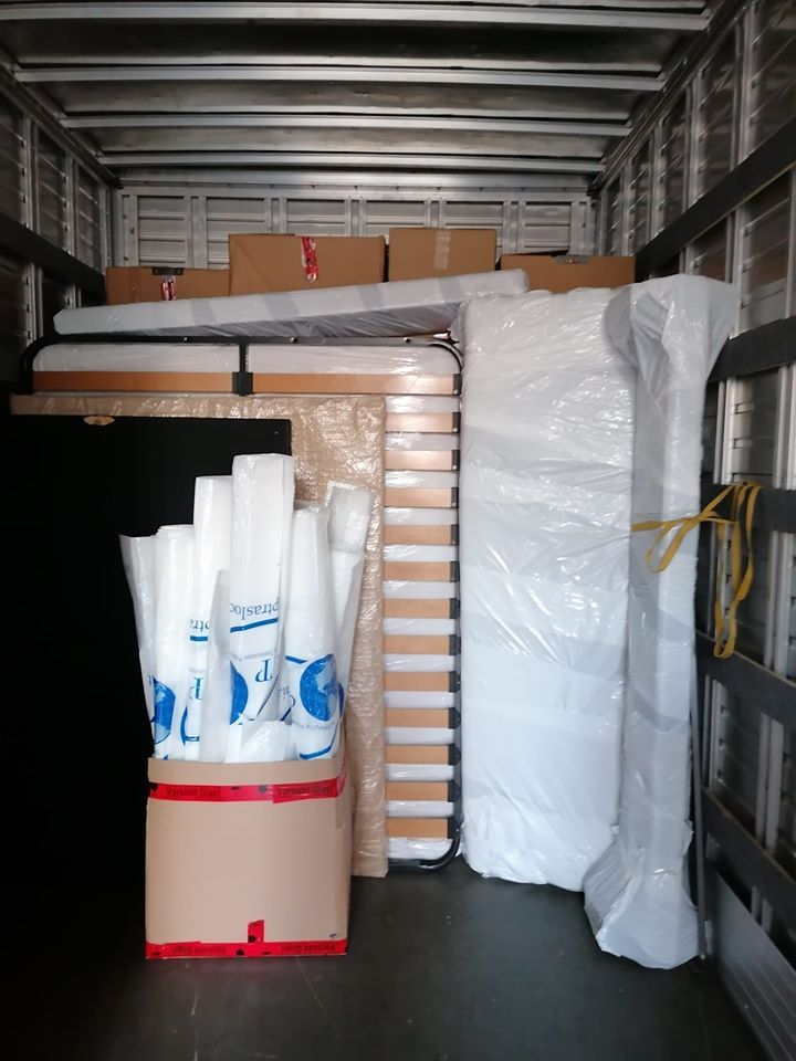 Camion per traslochi carico di scatole impilate, teli bianchi arrotolati e mobili imballati all'interno.