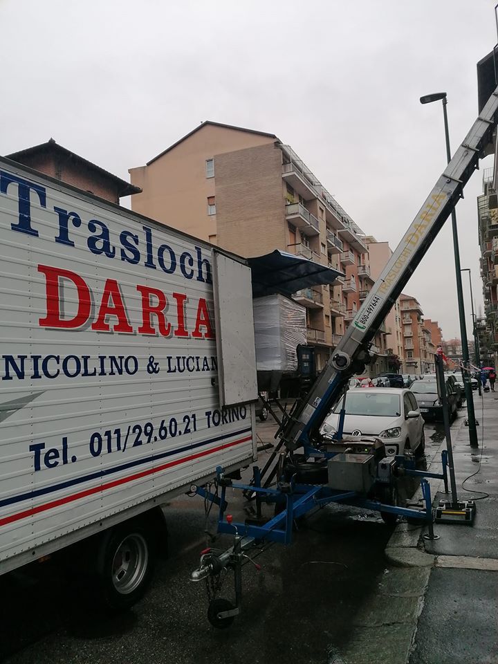 Camion per traslochi con gru su una stretta via cittadina accanto a palazzi residenziali.
