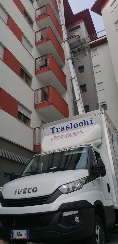 Un camion per traslochi IVECO bianco è parcheggiato accanto a un condominio rosso e grigio con l'insegna