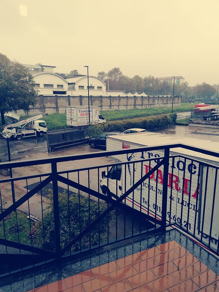 Vista sul lungomare sotto la pioggia da un balcone, con canale, auto parcheggiate ed edifici sotto un cielo grigio.