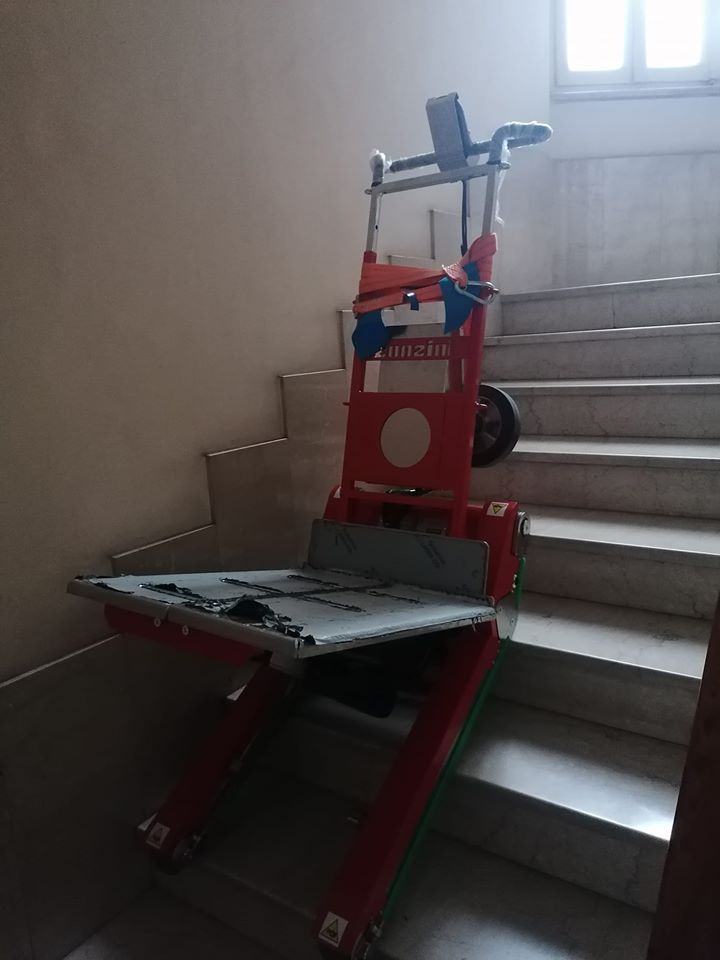 Una sedia a rotelle rossa per salire le scale è parcheggiata su una scala interna vicino a una finestra.
