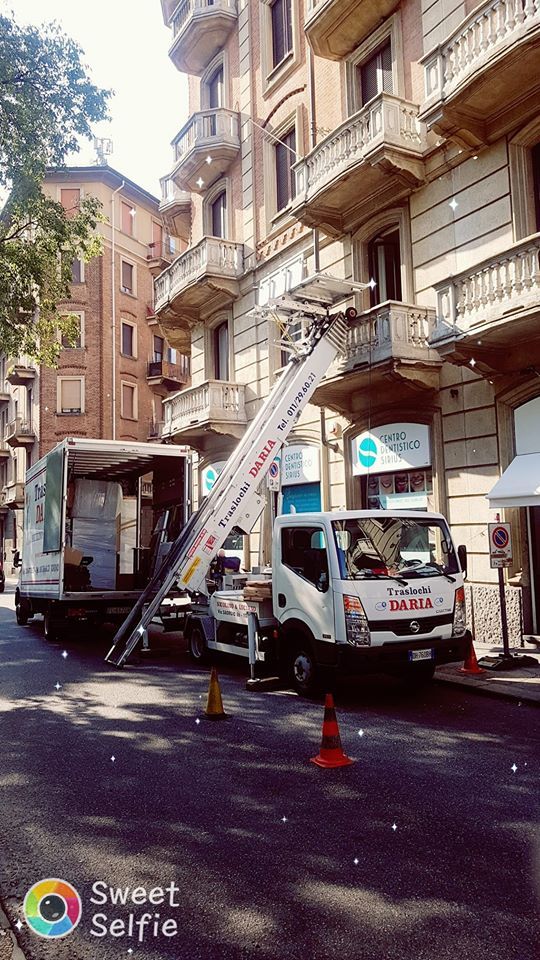 Camion con scala estensibile che solleva oggetti su una strada cittadina accanto a palazzi residenziali.