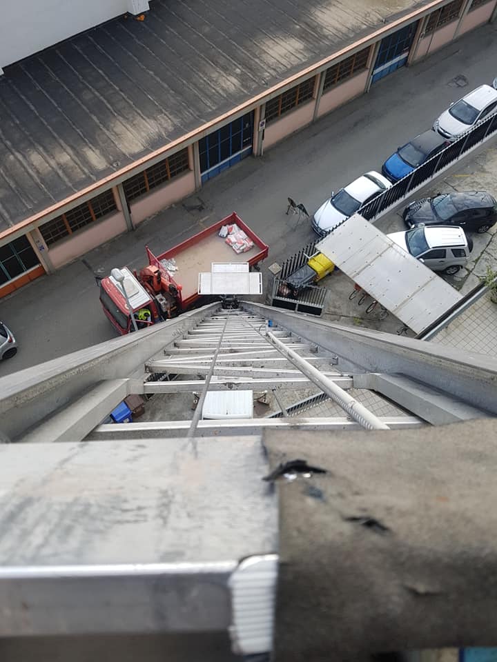 Vista dall'alto di una lunga scala su un parcheggio con auto parcheggiate e il tetto di un edificio sottostante.