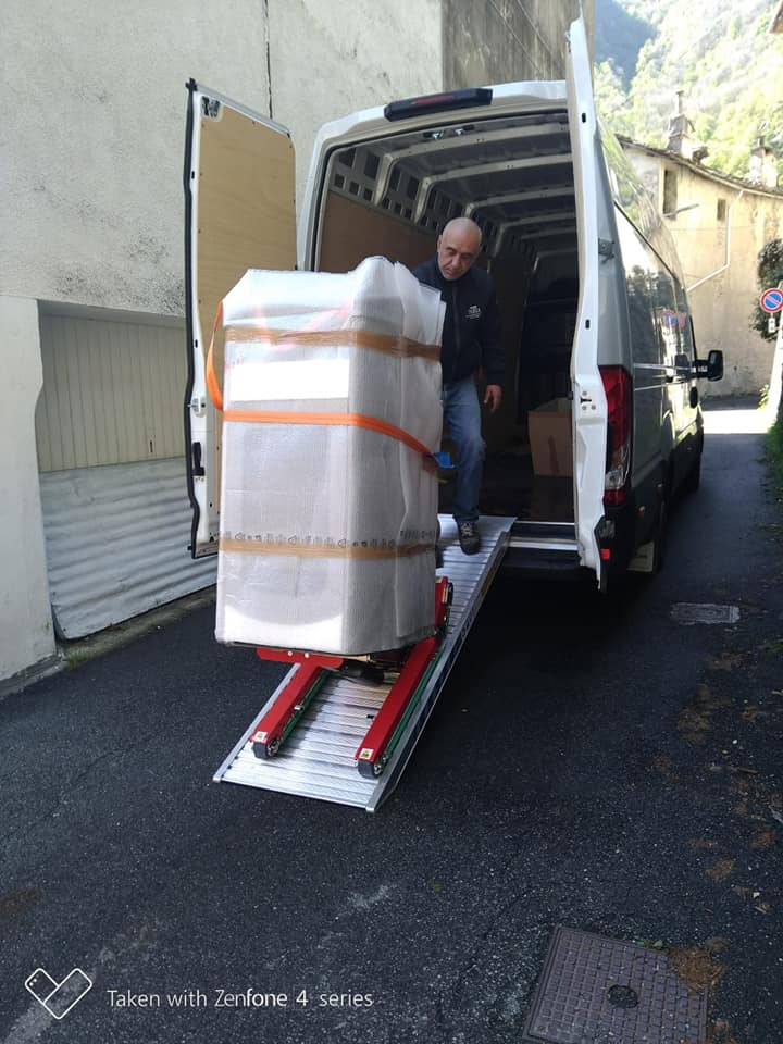 Un uomo scarica un grosso pacco avvolto da un furgone delle consegne lungo una rampa in strada.