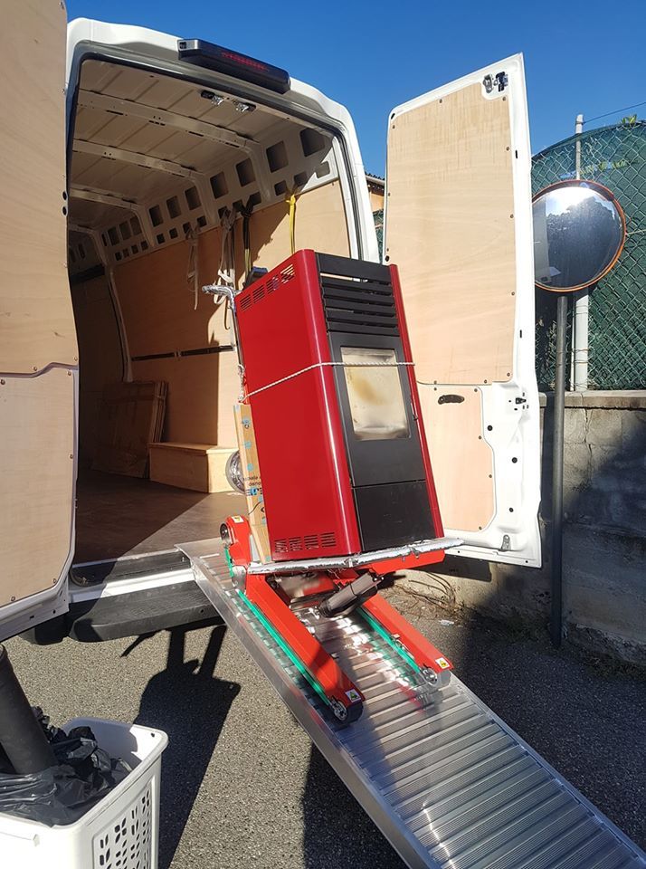 Un elettrodomestico rosso viene caricato su un furgone tramite una rampa metallica, con l'aiuto di un carrello a mano.