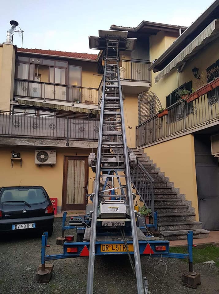 Autoscala estesa fino a una finestra del secondo piano in un cortile residenziale, con scale e auto parcheggiate nelle vicinanze.