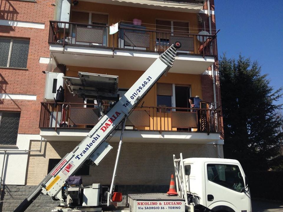 Piattaforma elevatrice per camion traslochi che si estende fino al balcone di un appartamento al terzo piano di un edificio residenziale.