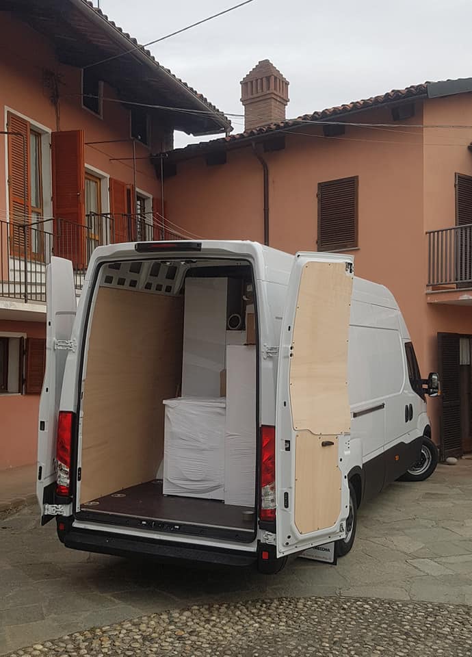 Furgone bianco per le consegne con portellone posteriore aperto, che mostra pacchi impilati in un cortile.