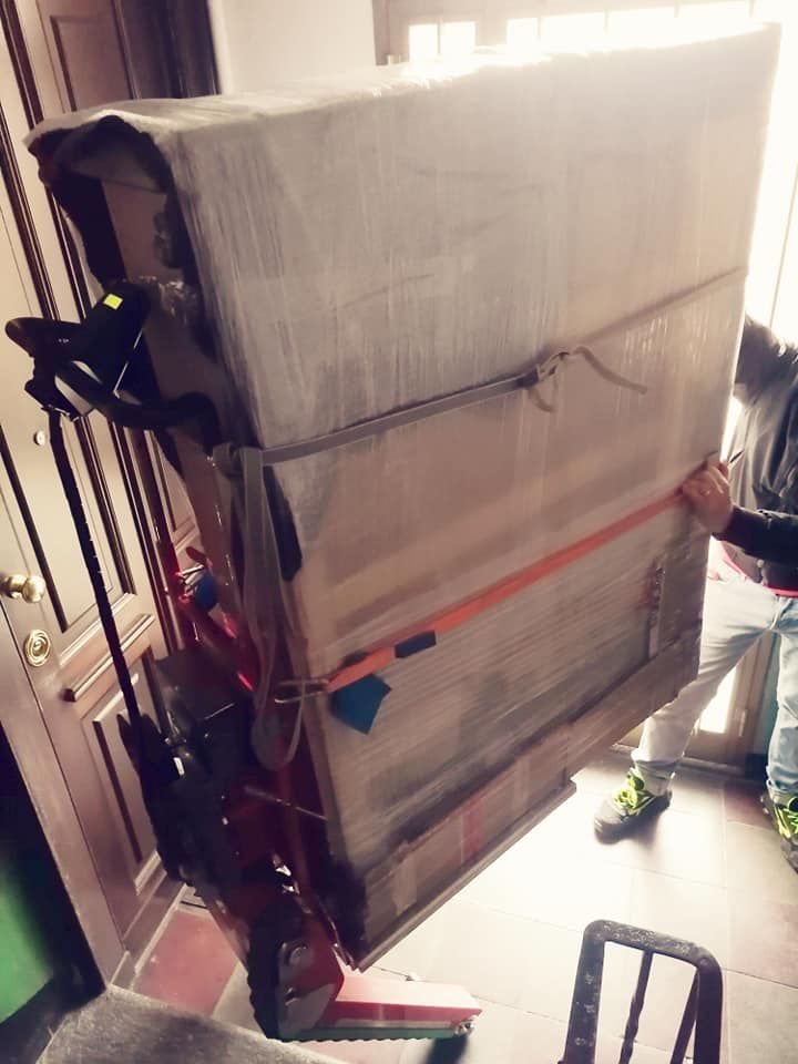 Un grosso pacco imballato viene trasportato attraverso una porta dai traslocatori con un carrello a mano.