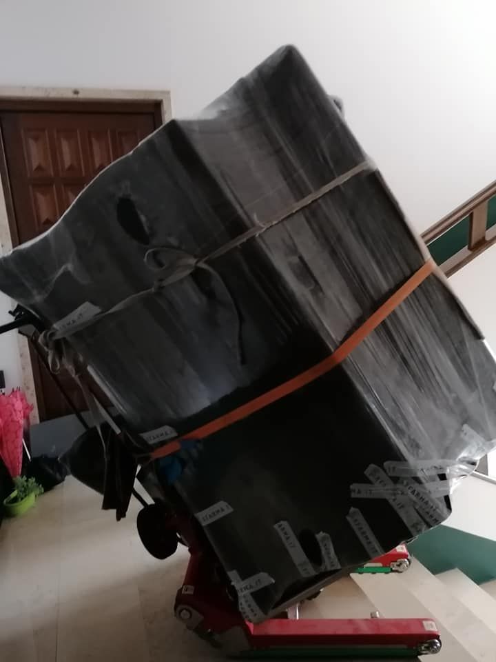 Un grande oggetto cilindrico nero, fissato a una piattaforma rossa e inclinato diagonalmente contro una parete bianca.