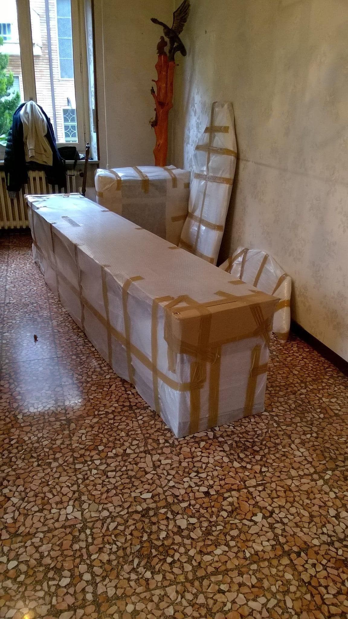 Panca avvolgente in un corridoio con finestra, sedia e scala addossate alla parete.