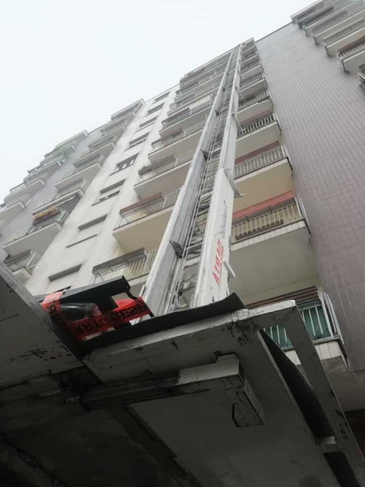 Vista dal basso di un alto condominio con balconi e un'auto parcheggiata in primo piano.