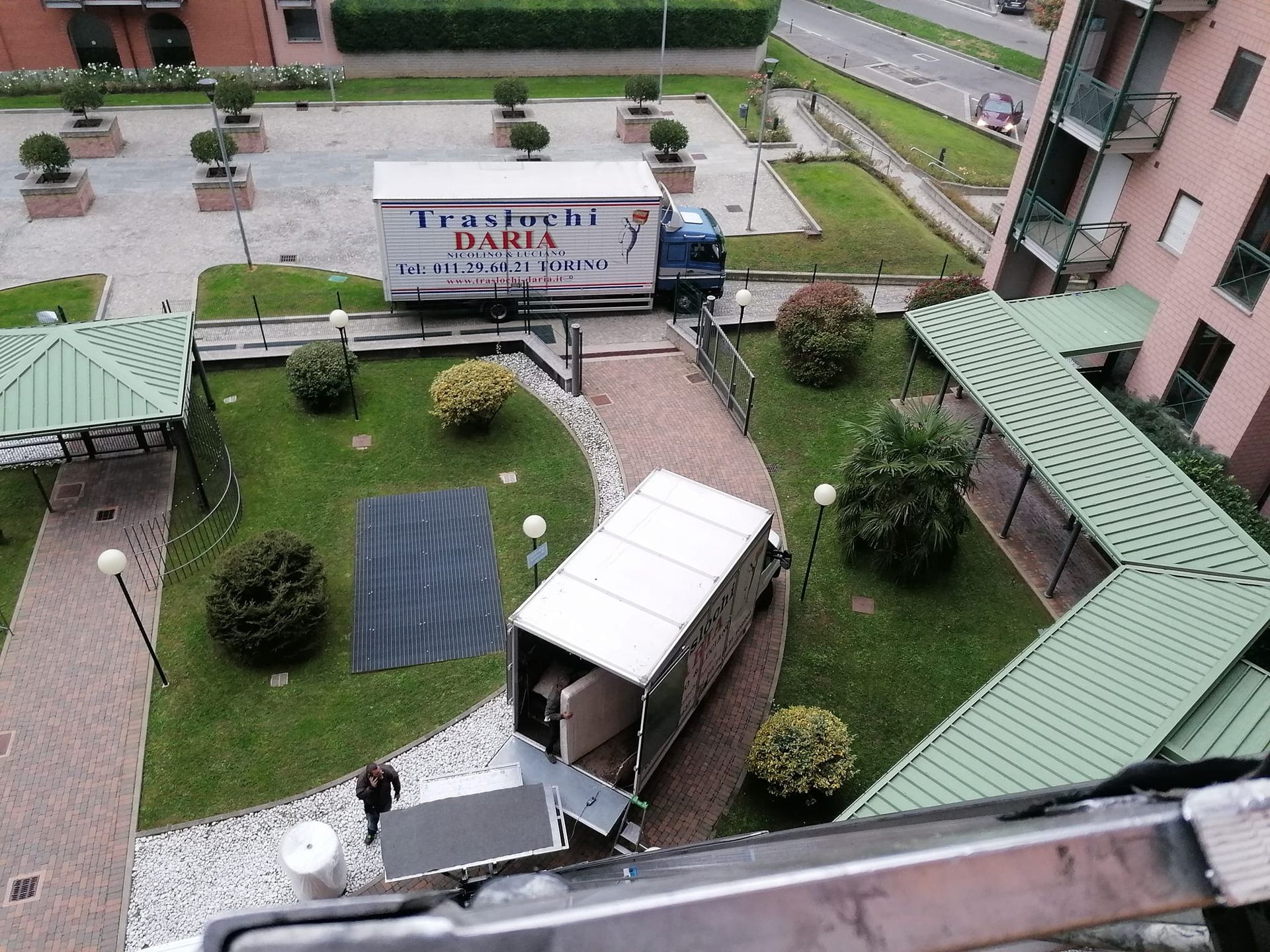 Cortile con tetti verdi, pannelli solari e un furgone bianco accanto a un cartello tra i palazzi.
