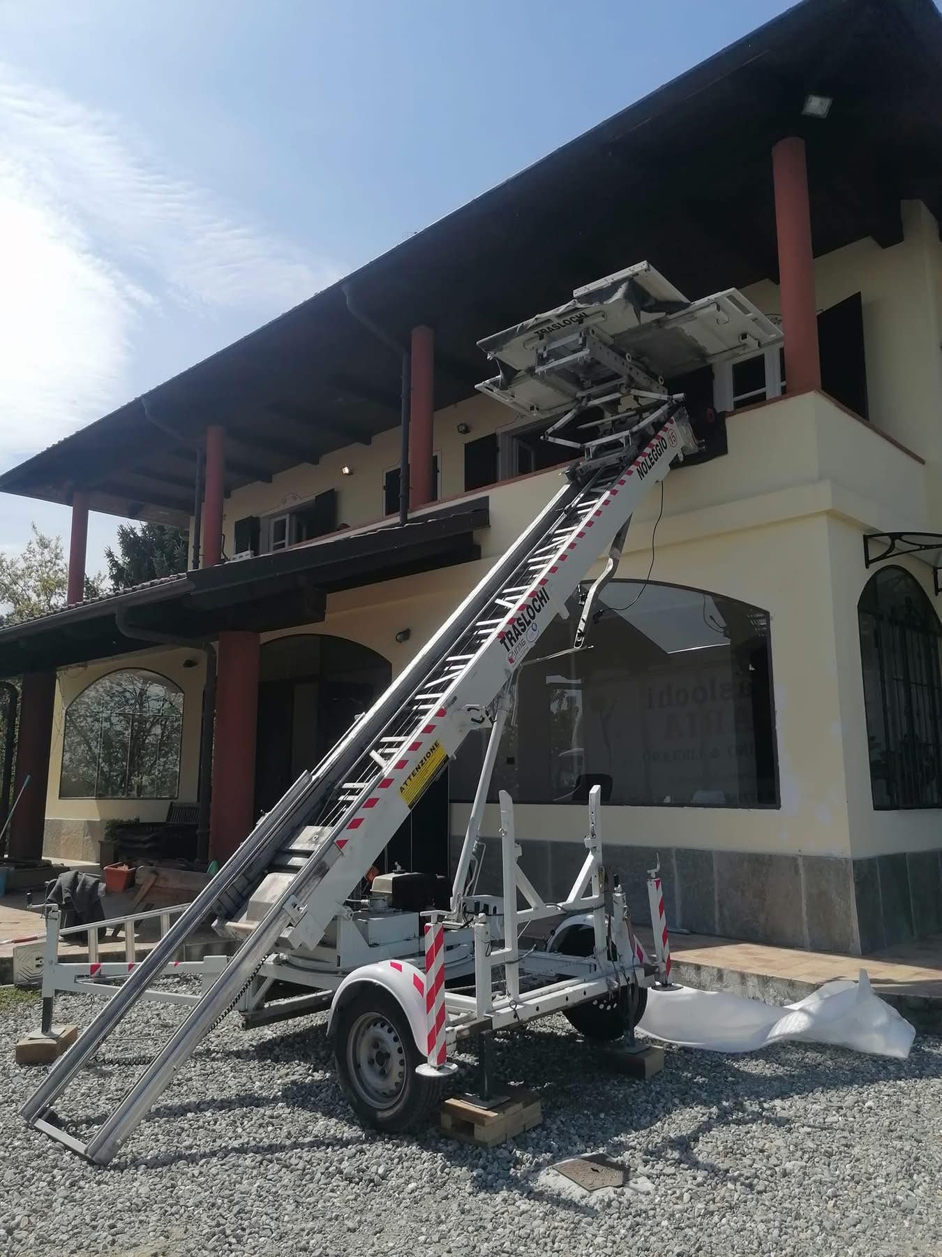 Autoscala estesa fino al tetto di un edificio a due piani con balconi e ingressi ad arco, attualmente in fase di riparazione.