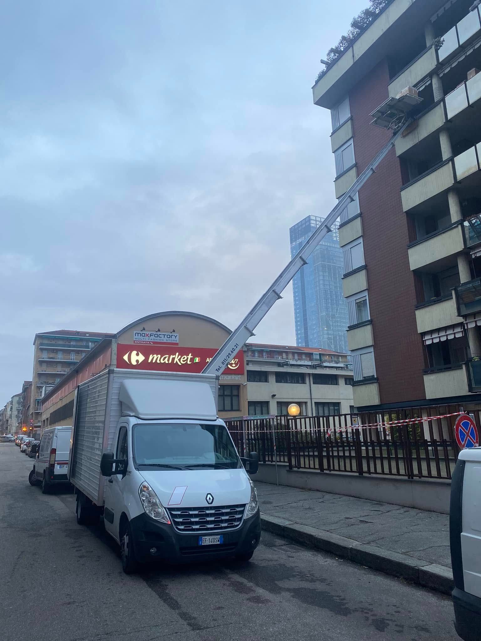 Un furgone bianco per le consegne parcheggiato in una strada cittadina accanto a un negozio e a un condominio al crepuscolo.