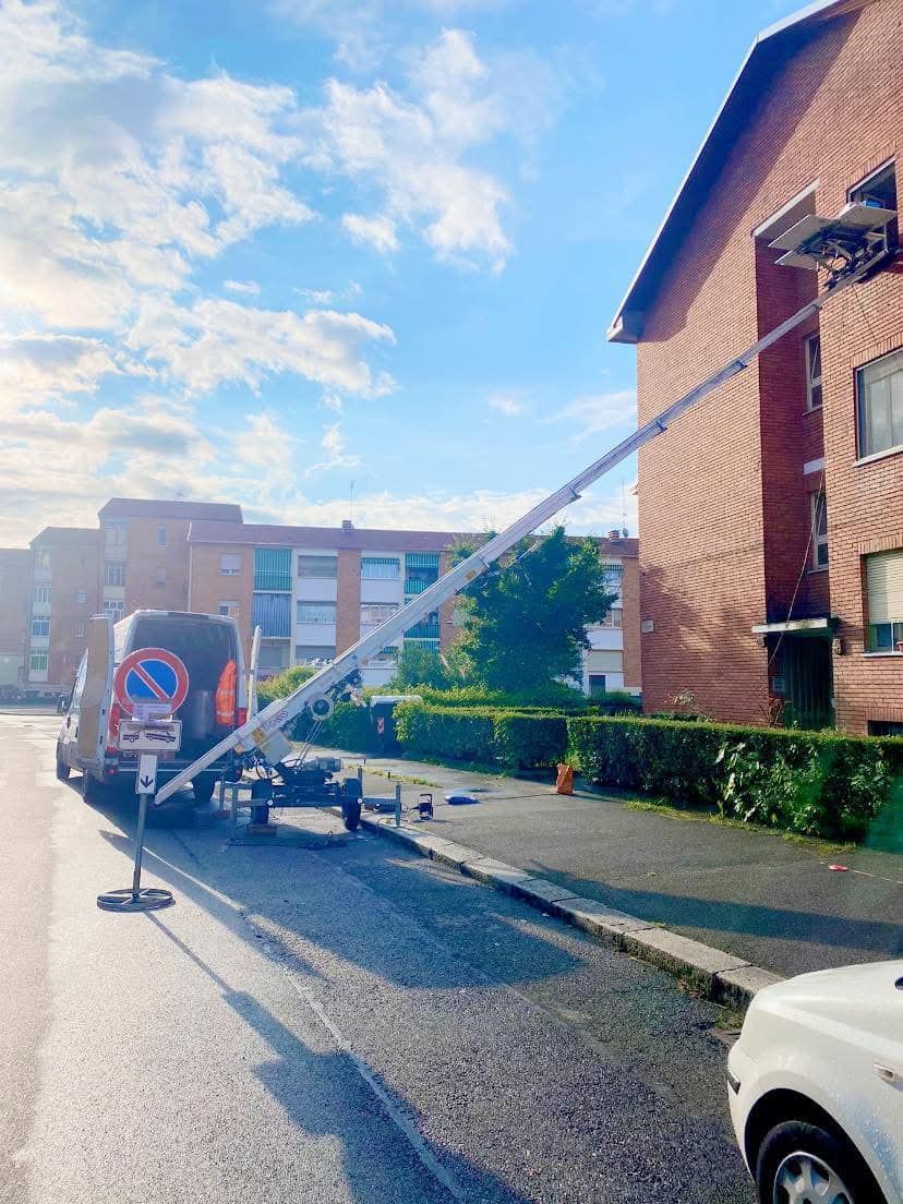 Scena di strada con un camion di servizio e un braccio meccanico sollevato vicino a un edificio in mattoni rossi in una giornata di sole.