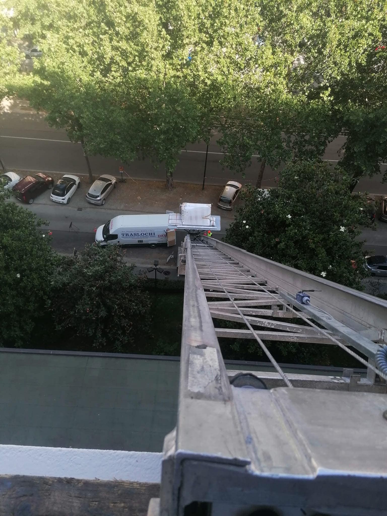 Vista da una scala alta verso un furgone bianco parcheggiato vicino ad alberi e un marciapiede.