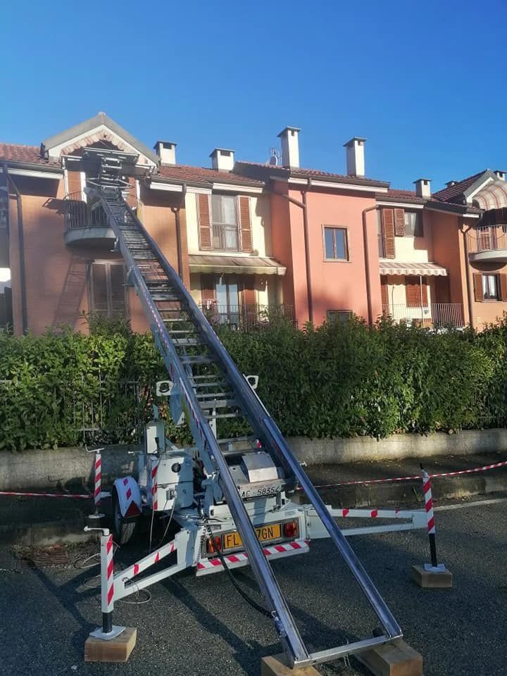 Piattaforma di lavoro sopraelevata con scala sollevata accanto a un condominio rosa sotto un cielo azzurro.