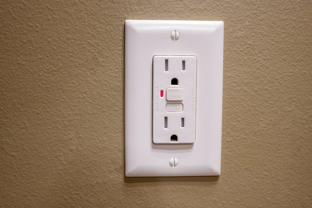 Electrician is using a digital meter to measure the voltage at the power outlet in on the wall.
