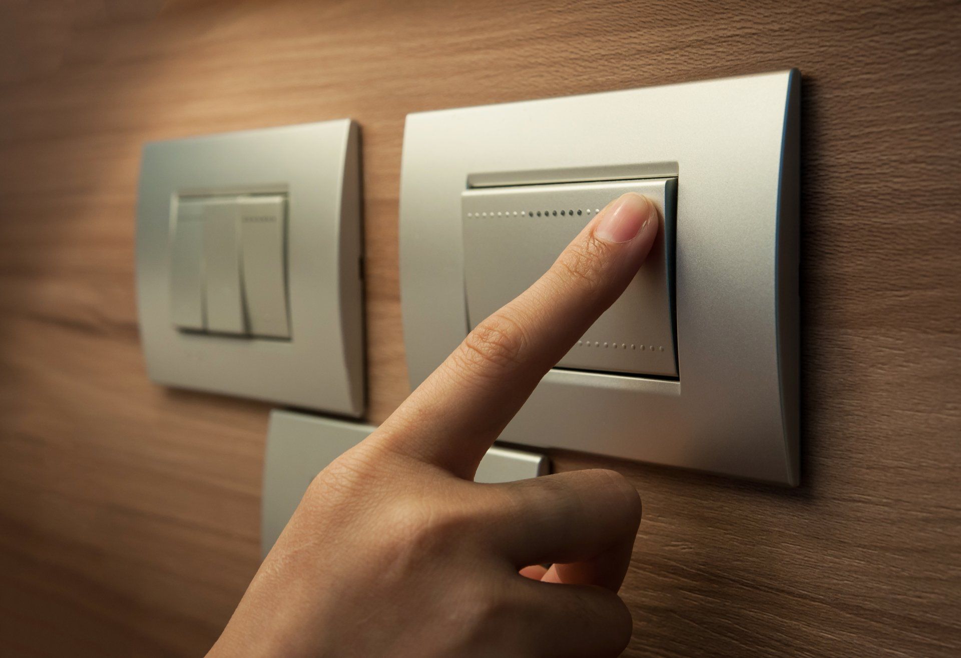 Close up of male finger is turn off on grey button of light switch over wood wall at home.