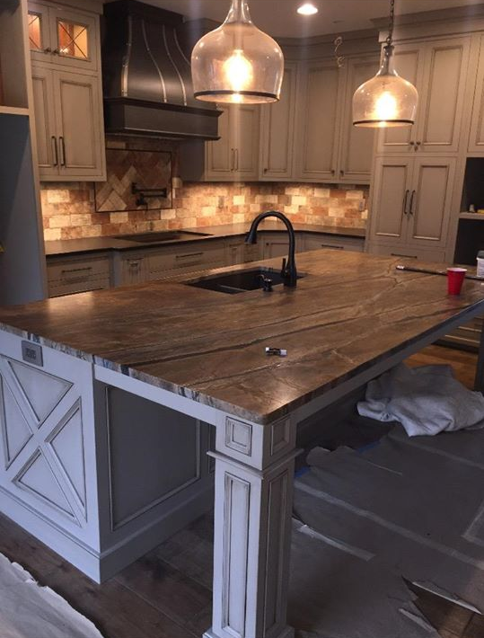 Kitchen with gray cabinets, a large island with a brown countertop, and pendant lights.