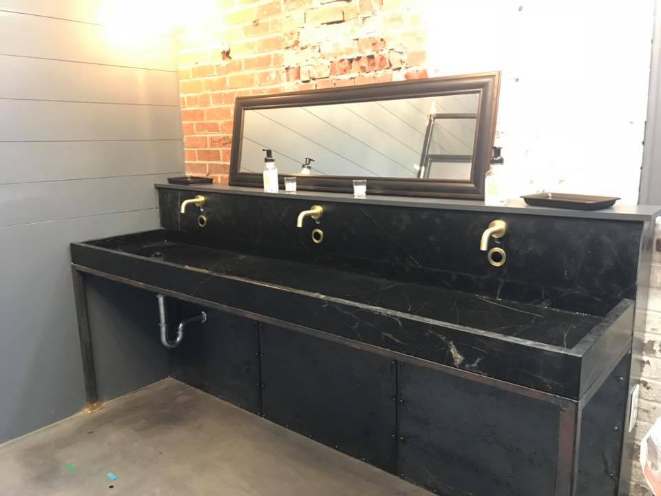 Bathroom with black sinks, gold faucets, a large mirror, and brick wall.