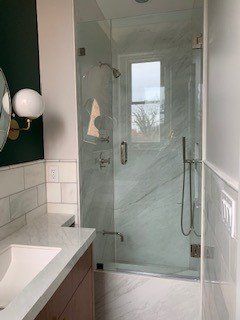 Shower with glass doors and marble-look walls; window and shower fixtures visible.