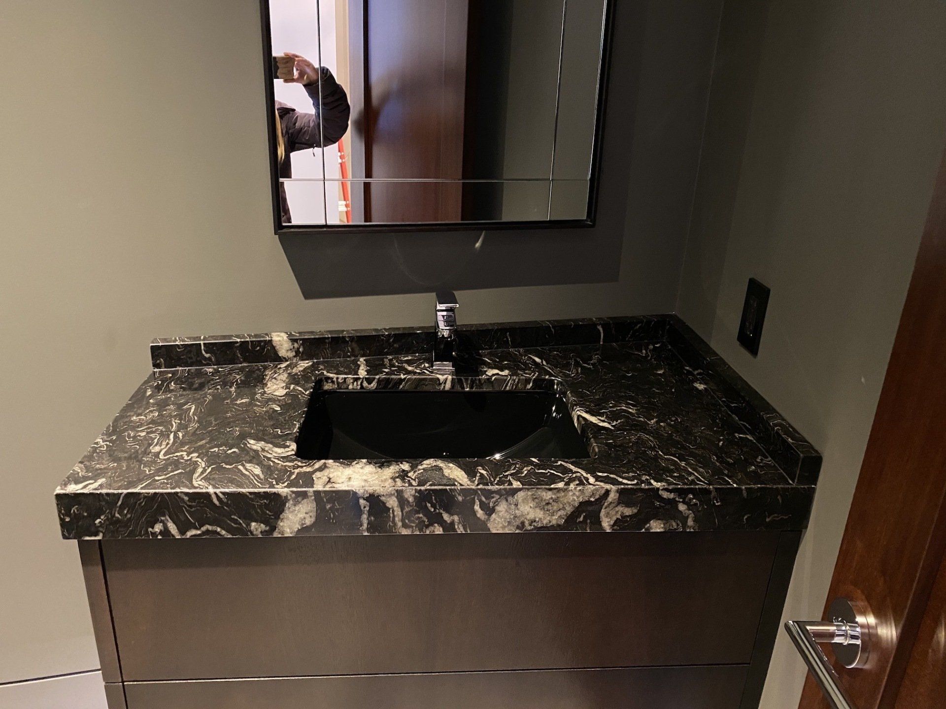 Bathroom vanity with black and white countertop, black sink, mirror, and dark gray cabinet.