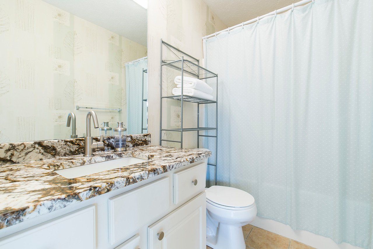 Bathroom with white cabinets, patterned countertop, and a white shower curtain.